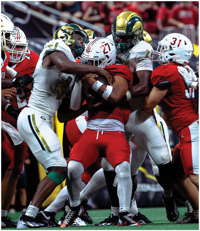 Several people in football uniforms are engaged in a close physical struggle on a field during a game. Description generated by AI
