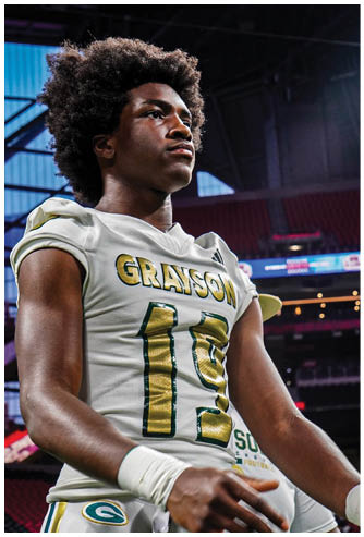 A person wearing a white football jersey with the name Grayson and the number 12 stands in a stadium with a focused expression. Description generated by AI