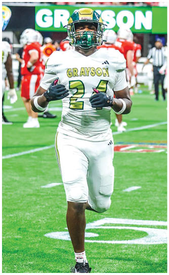 A person in a white football uniform with the name “Grayson" and number 24 is running on a football field with other players and a crowd in the background. Description generated by AI