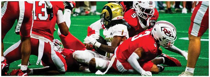 Several people in red and white sports uniforms are lying on a green field, appearing to be in the middle of a football play. Description generated by AI