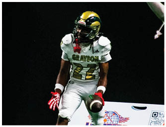 A person in a white football uniform with the number 22 is holding a football while two other players in different colored uniforms are nearby on a football field. Description generated by AI