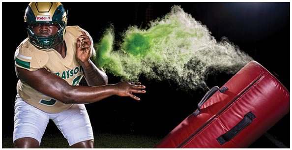 A person is reaching up with one hand toward a cloud of green powder or smoke near a red punching bag against a dark background. Description generated by AI