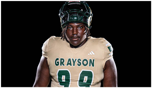 A person wearing a football helmet and a beige jersey with the name Grayson and the number 99 on it is looking forward against a black background. Description generated by AI