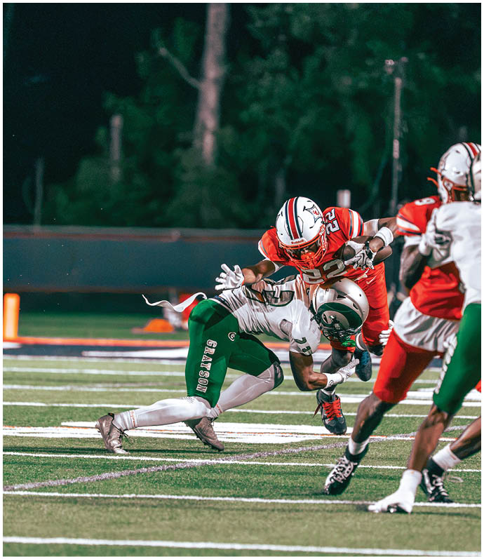 Two people in football uniforms are engaged in a tackle on a field during a game, with one player in red attempting to evade a player in green. Description generated by AI