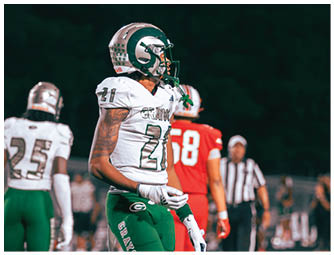 A person wearing a white and green football uniform with the number 21 is in the foreground while another person in a red football uniform with the number 58 and a referee are in the background. Description generated by AI