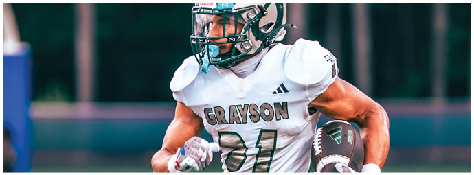 A person wearing a white football uniform with “GRAYSON" on the chest is running while holding a football on a field. Description generated by AI