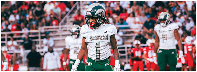 A person wearing a white football uniform with the word Grayson and the number 1 stands on a field with other players and a crowd in the background. Description generated by AI