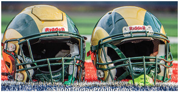 Two football helmets with green and yellow designs are placed side by side on a field. Description generated by AI