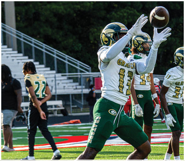 People wearing green and white football uniforms are on a field with bleachers and a fence in the background. Description generated by AI