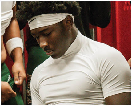 A person with curly hair wearing a white headband and white athletic clothing is looking downward with a focused expression. Description generated by AI