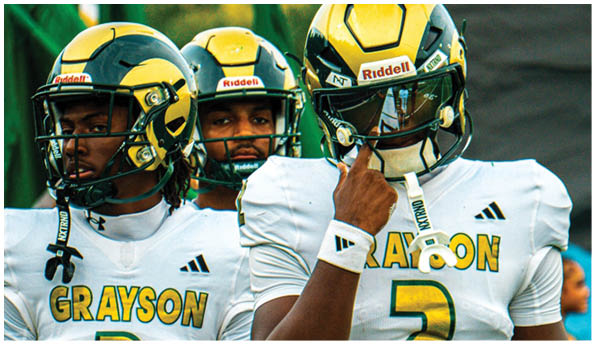Three people wearing yellow and green football helmets stand closely together outdoors with green flags and trees in the background. Description generated by AI