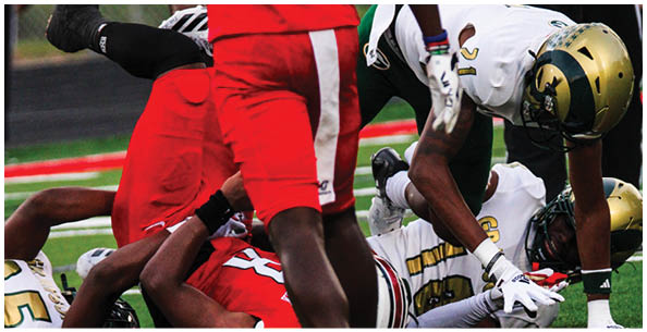 Several people in football uniforms are engaged in a play on a field, with some lying on the ground and others reaching toward each other. Description generated by AI