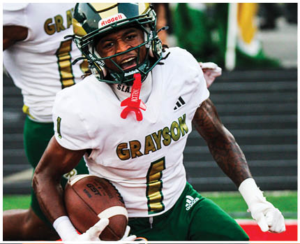 A person wearing a gold and black football helmet and a white jersey with “GRAYSON" written on it is celebrating energetically on a football field. Description generated by AI