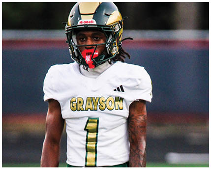 A person wearing a white football uniform with the word Grayson and the number one on the front stands on a field wearing a black and gold helmet with a red mouthguard. Description generated by AI