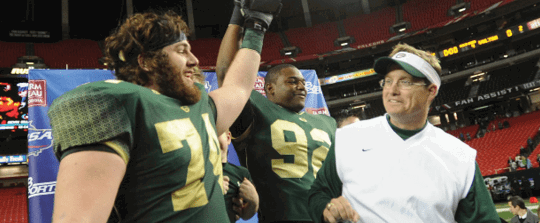 Three people in football uniforms and gear are celebrating together inside a stadium. Description generated by AI