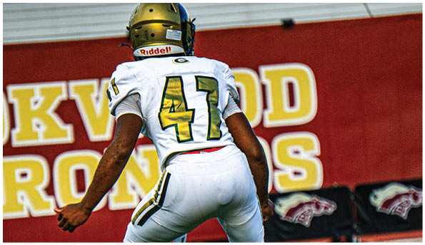 A person wearing white athletic pants and cleats is standing on a green football field with white yard lines. Description generated by AI