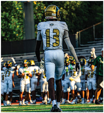 A person wearing a white football uniform with the number 13 is walking on a field toward a group of similarly dressed players standing on the sidelines. Description generated by AI
