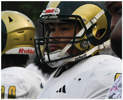 A person wearing a football helmet and white jersey is standing next to others in similar gear during a game or practice. Description generated by AI
