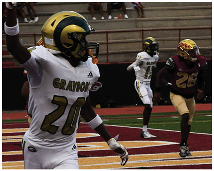 A person in a white football uniform with “GRAYSON" on the jersey is celebrating on a football field while two other players in maroon and gold uniforms are in the background. Description generated by AI