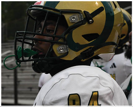 A person wearing a yellow and green football helmet with a black faceguard and a green mouthguard. Description generated by AI