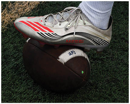 A close-up of a brown American football resting on green artificial turf. Description generated by AI