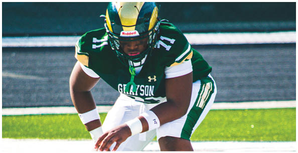 A person wearing a green and white football uniform is crouched on a field, preparing to snap the ball. Description generated by AI