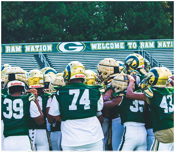 A group of people wearing green and white football uniforms and helmets are huddled together on a field. Description generated by AI