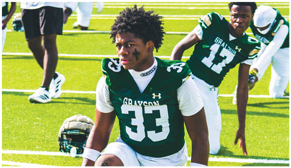 A person wearing a green and white football uniform with the number 33 is kneeling on a grassy field with a helmet placed on the ground nearby. Description generated by AI