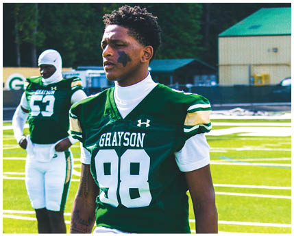 Two people wearing green and white football uniforms with “GRAYSON" and numbers on the front stand on a football field with one person in the foreground and the other in the background. Description generated by AI