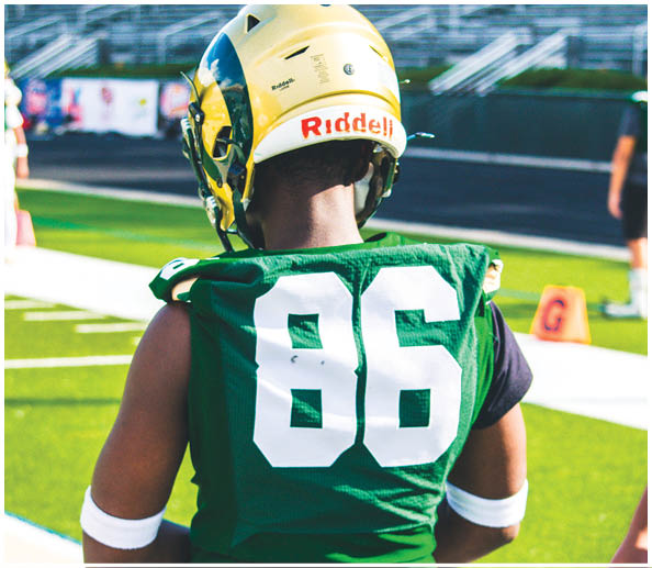 A person wearing a green football jersey with the number 86 and a yellow helmet stands on a football field. Description generated by AI