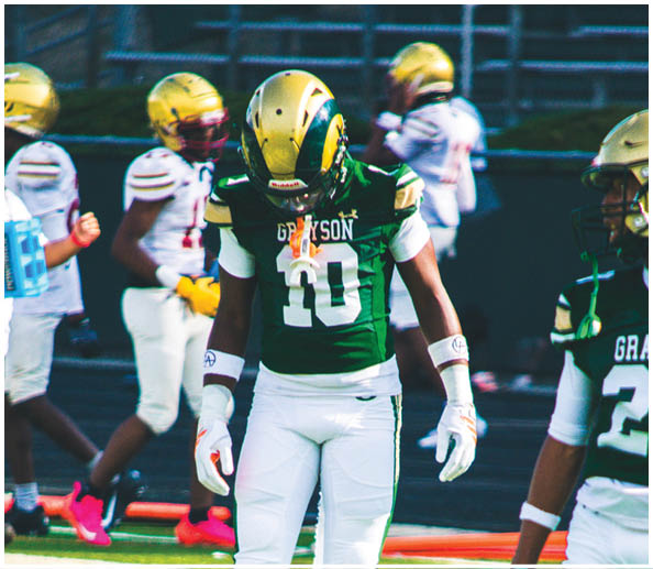 Two people wearing green and white football uniforms stand on a field with one person wearing white gloves and the other wearing blue gloves. Description generated by AI