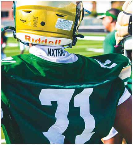 A person wearing a green sports jersey with the number 71 and white gloves is standing on a field. Description generated by AI