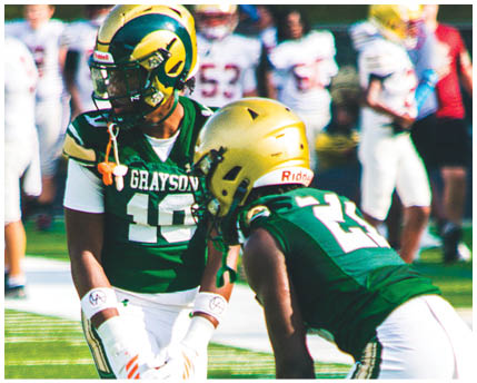 Two people in green and white football uniforms are standing on a field with one person bent forward and the other standing upright holding a football. Description generated by AI