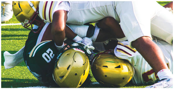 Several people wearing football helmets and uniforms are engaged in a tackle on a grassy field. Description generated by AI