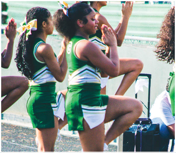 People in green and white cheerleading uniforms are performing a routine outdoors on a track with pom-poms on the ground nearby. Description generated by AI