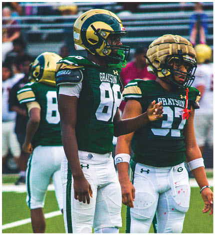 People wearing green and white football uniforms standing on a field, with one person gesturing with their hand. Description generated by AI