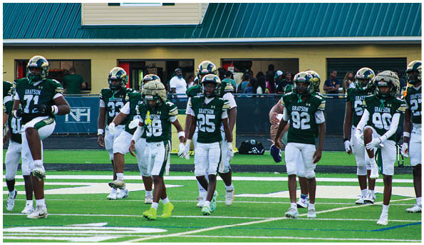 A group of people wearing green and white football uniforms are standing and walking on a football field. Description generated by AI