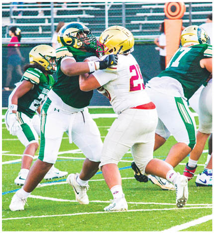 Two people in football uniforms are engaged in a blocking action on a green field while another player stands nearby. Description generated by AI
