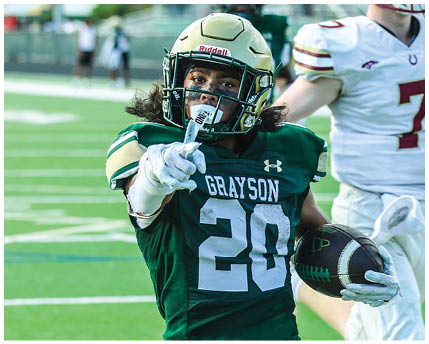 A person wearing a green football uniform with the name Grayson and number 20 is pointing forward on a football field. Description generated by AI