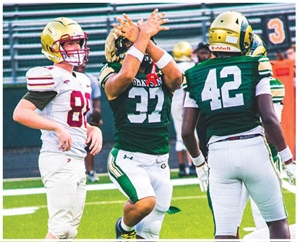 Three people wearing sports uniforms stand on a green field with one person in mid-step and another person crouching. Description generated by AI