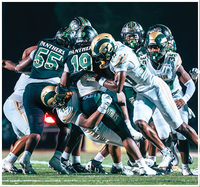 A group of people wearing football uniforms are on a field with one person in a white and green uniform standing in the center and others in red uniforms around them. Description generated by AI