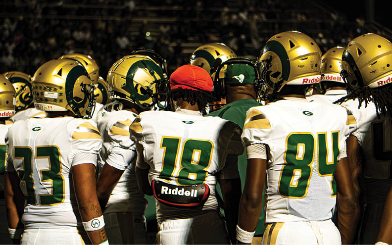 Four people wearing white and green football uniforms stand side by side with their backs facing the camera. Description generated by AI