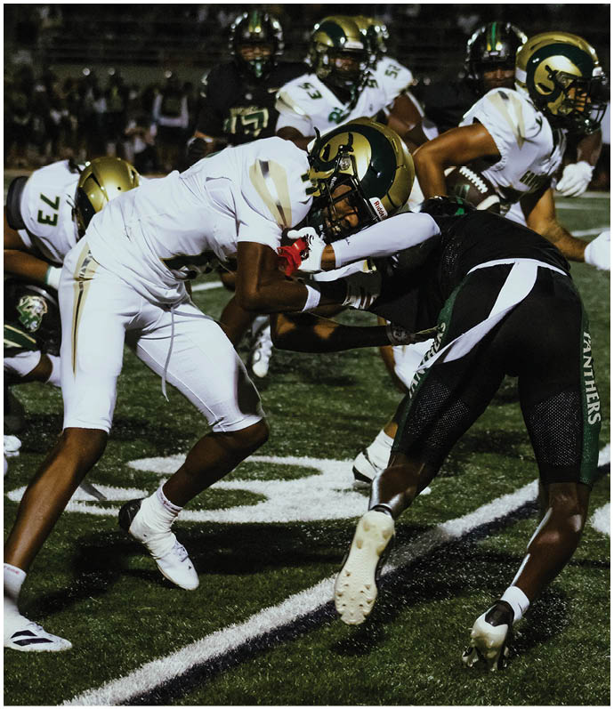 Several people in football uniforms are lined up on a field facing each other, preparing for a play during a game with spectators in the background. Description generated by AI