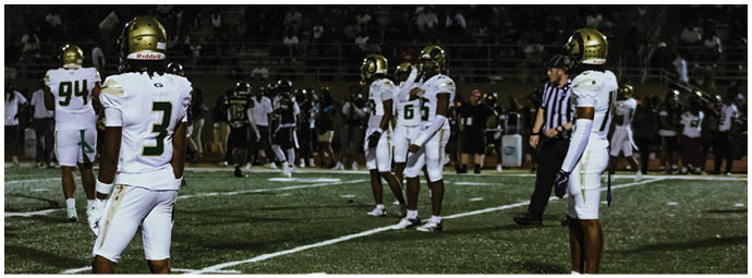 Two people wearing football helmets are positioned on a field under a goalpost. Description generated by AI