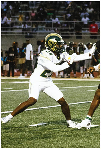 A person wearing a football uniform with a helmet and gloves is standing on a football field during a game. Description generated by AI