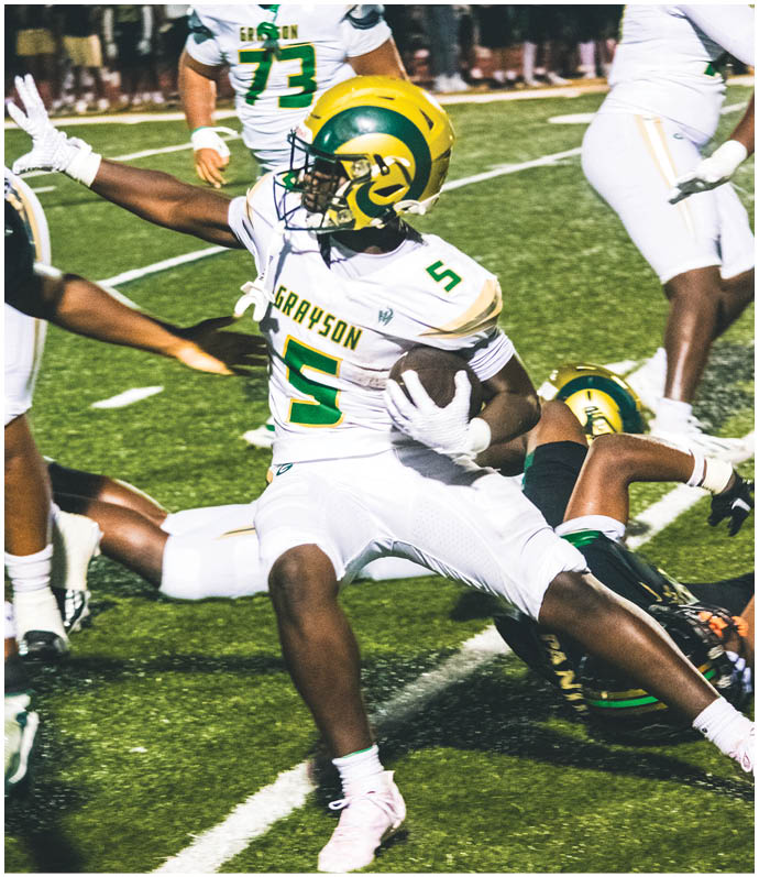 Two people in football uniforms are engaged in a tackle on a field during a game, with one player in red attempting to evade a player in green. Description generated by AI