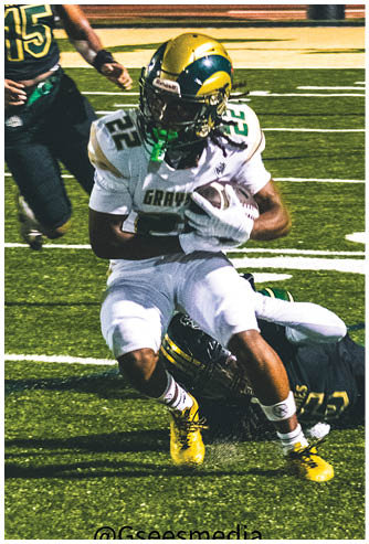 A person in a red football uniform is running with the ball while another person in a white and green uniform lunges forward attempting to tackle them on a football field. Description generated by AI