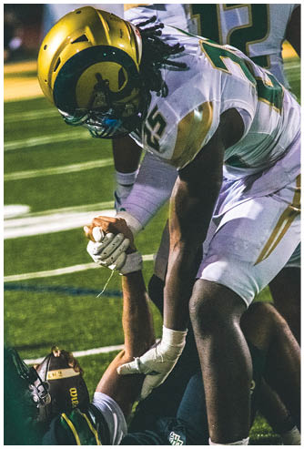 Two people in football uniforms are engaged in a tackle on a field during a game at night. Description generated by AI