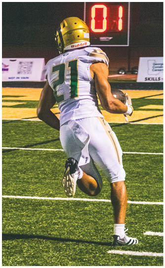 Two people in football uniforms and helmets are positioned on a field with one crouching and holding a football while the other stands behind. Description generated by AI
