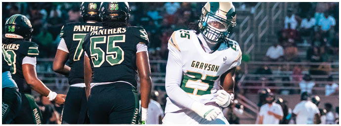 A person wearing a white football uniform with the word Grayson and the number 1 stands on a field with other players and a crowd in the background. Description generated by AI